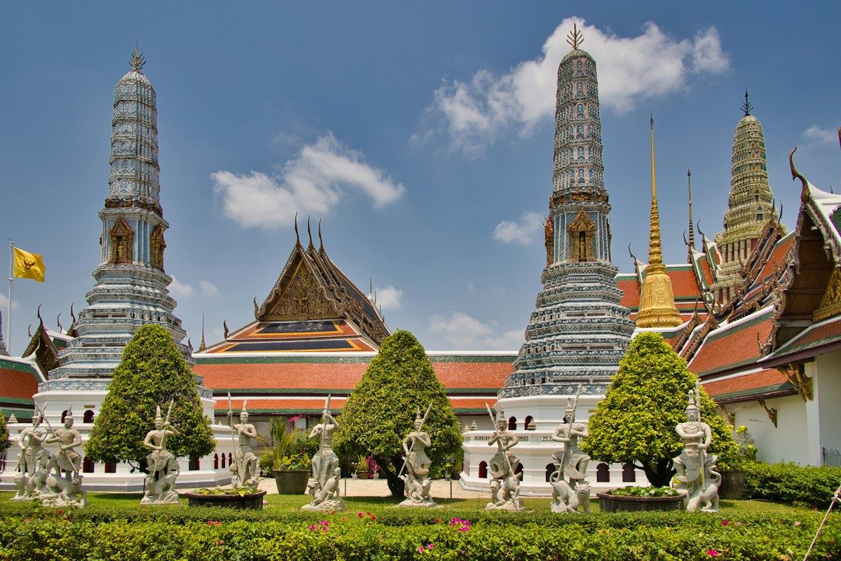 Tempelanlegg med hvite stupaer og grønne trær i Bangkok som illustrasjon på å flytte til Thailand
