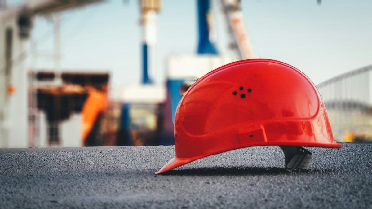 Rød vernehjelm som ligger på asfalten som illustrasjon på yrkesskade og arbeidsulykker