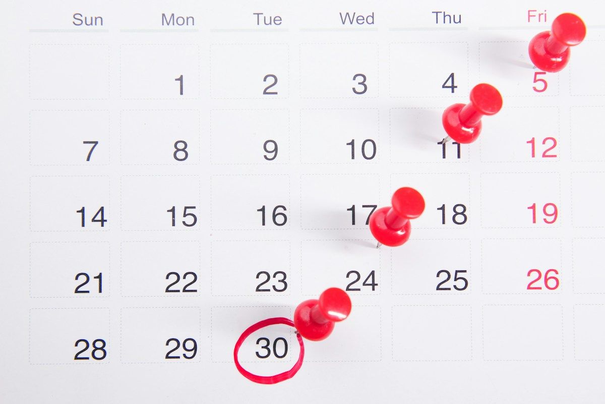 Kalender med røde knappenåler festet på datoer som illustrasjon på etterbetaling