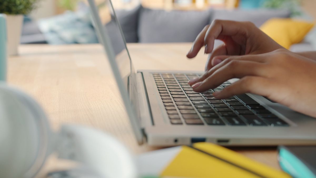 Hender som skriver på en laptop ved skrivebordet