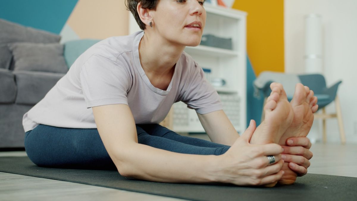 Kvinne toyer beina pa en yogamatte hjemme